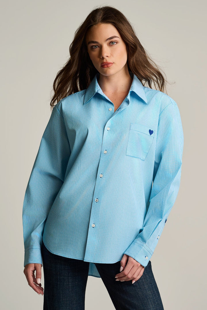 Woman wearing a light blue shirt with a small heart emblem on a plain background