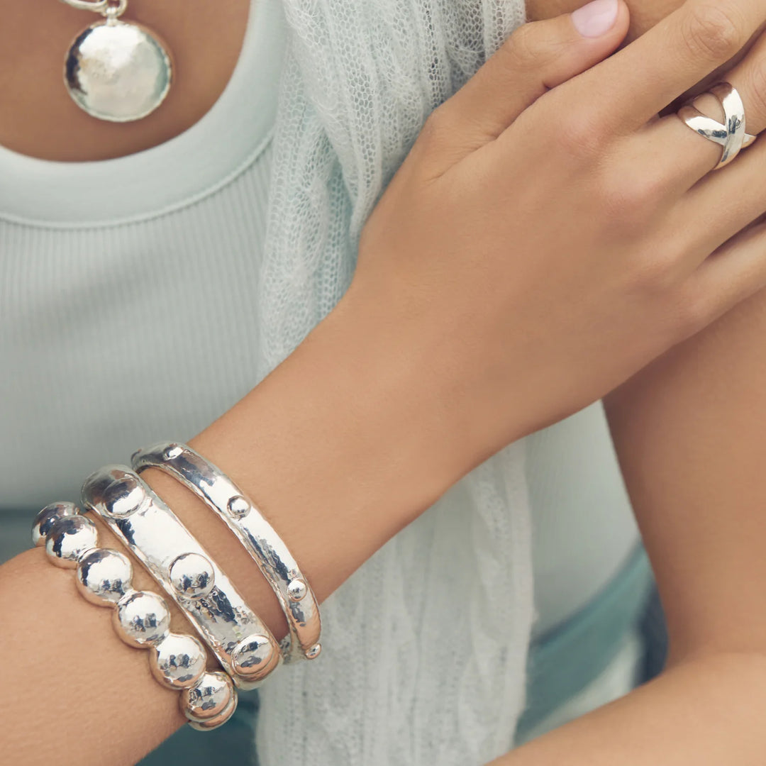 Julie Vos Solara Hinge Bangle in silver plate with hammered finish, dome stud accents, and engraved interior lattice pattern on model with multiple bracelets