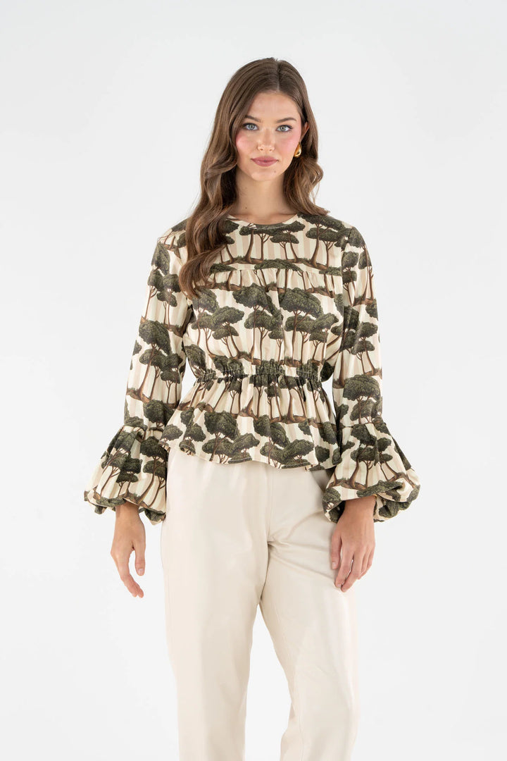 Woman wearing the Umbrella Pine print Harper Top with bubble-hem sleeves and cream trousers.