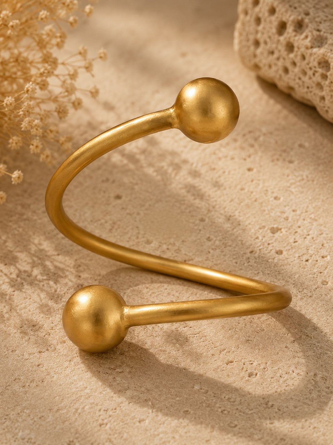 Front/hero shot — FLIP Gold Bracelet by Ximena Castillo, matte 24k gold-plated bronze spiral cuff on natural stone surface