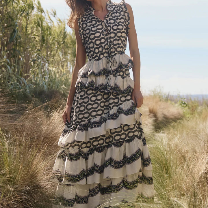 Woman in a patterned dress standing in a natural setting with greenery and blue sky.