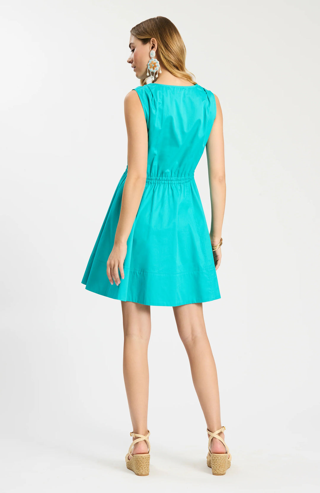 Model wearing Tyler Boe Emory Sleeveless Wrap Dress in teal, back view, styled with espadrille wedge sandals and floral drop earrings, on white background. - back