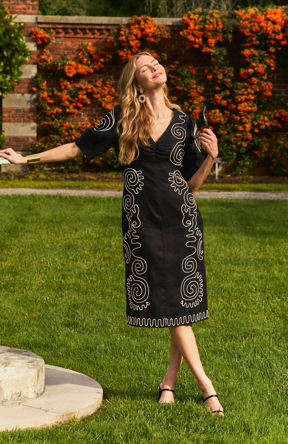 Model wearing Tyler Boe Posey Linen Embroidered Midi Dress in black with cream spiral cord embroidery, styled with black espadrille wedge sandals and gold necklace, full-length front view outside.