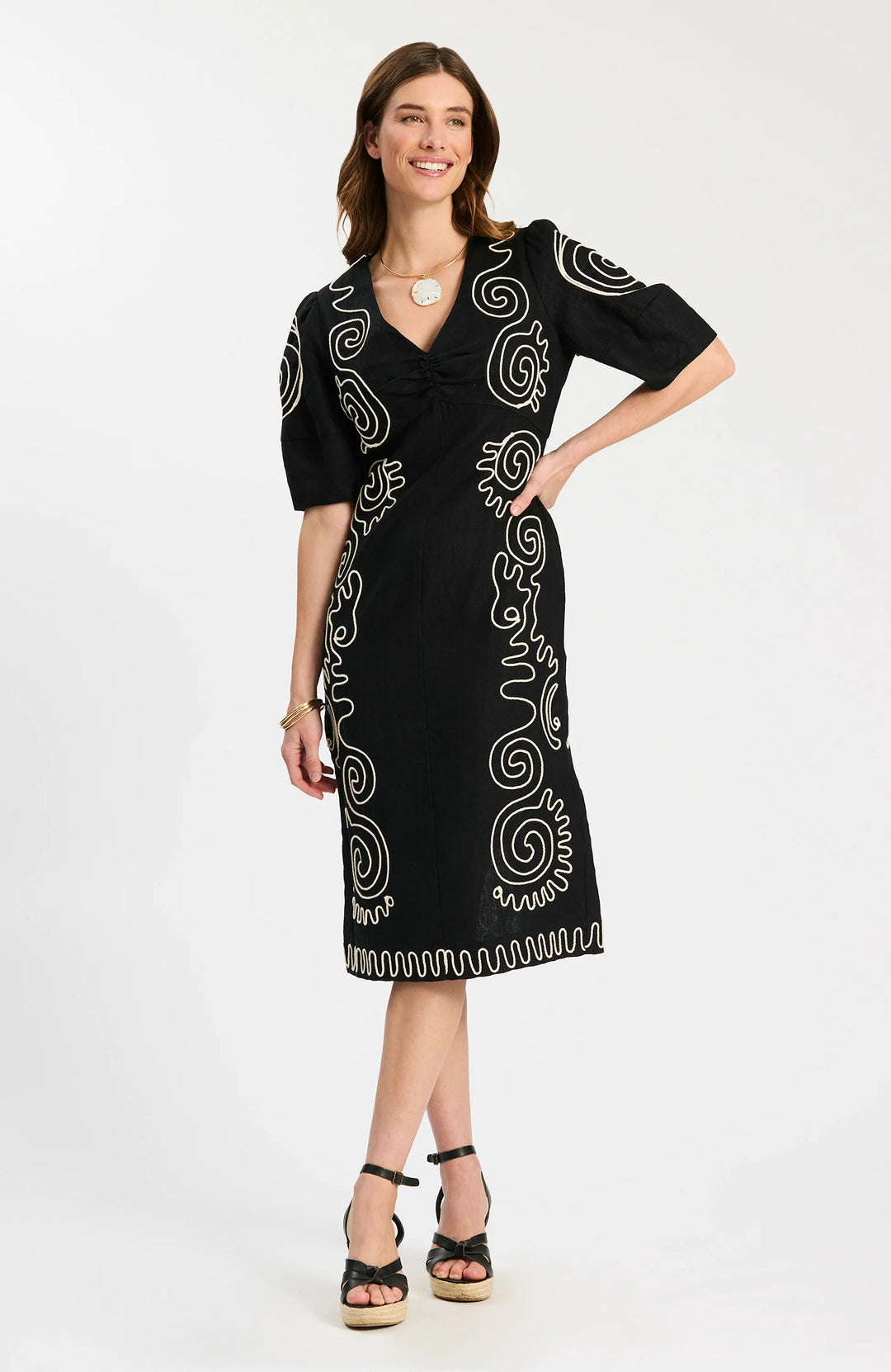Model wearing Tyler Boe Posey Linen Embroidered Midi Dress in black with cream spiral cord embroidery, styled with black espadrille wedge sandals and gold necklace, full-length front view on white background.