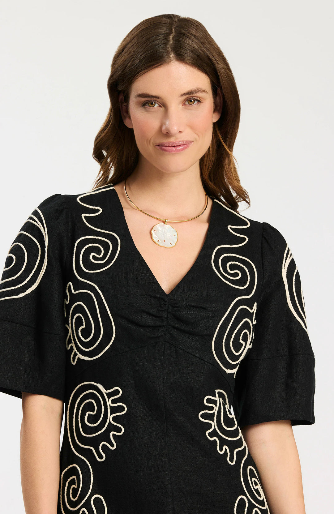 Model wearing Tyler Boe Posey Linen Embroidered Midi Dress in black with cream spiral cord embroidery, styled with black espadrille wedge sandals and gold necklace, full-length front view on white background. - top of dress