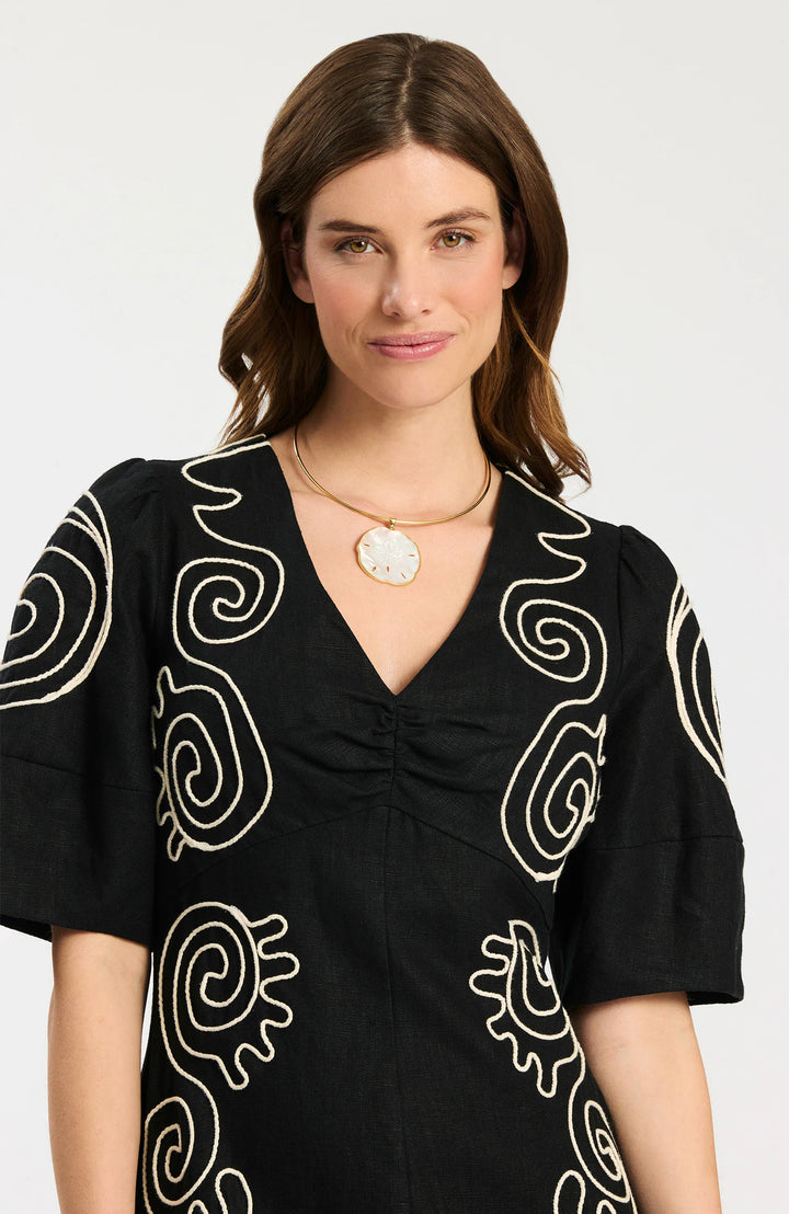 Model wearing Tyler Boe Posey Linen Embroidered Midi Dress in black with cream spiral cord embroidery, styled with black espadrille wedge sandals and gold necklace, full-length front view on white background. - top of dress