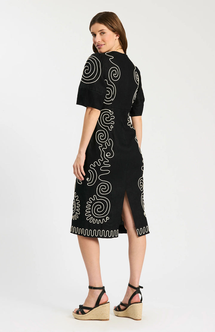 Model wearing Tyler Boe Posey Linen Embroidered Midi Dress in black with cream spiral cord embroidery, styled with black espadrille wedge sandals and gold necklace, full-length front view on white background. - back