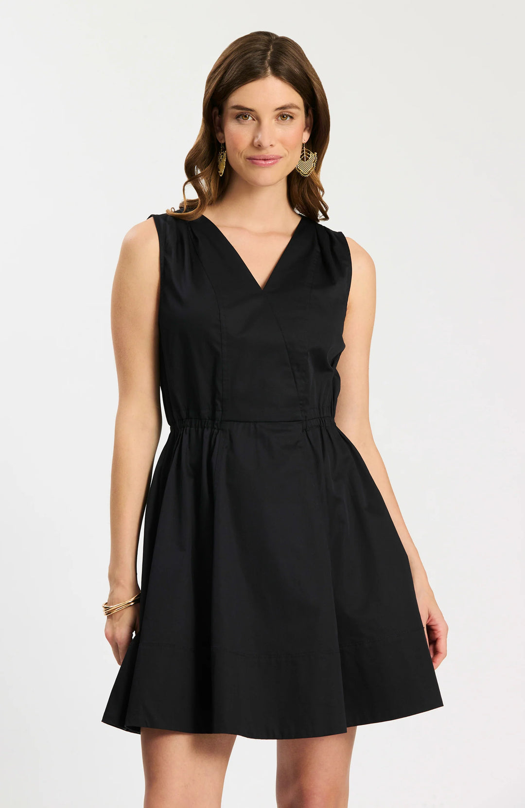 Model wearing Tyler Boe Emory Sleeveless Wrap Dress in black, front view belted with woven rattan belt, styled with black block-heel sandals and gold earrings, on white background.