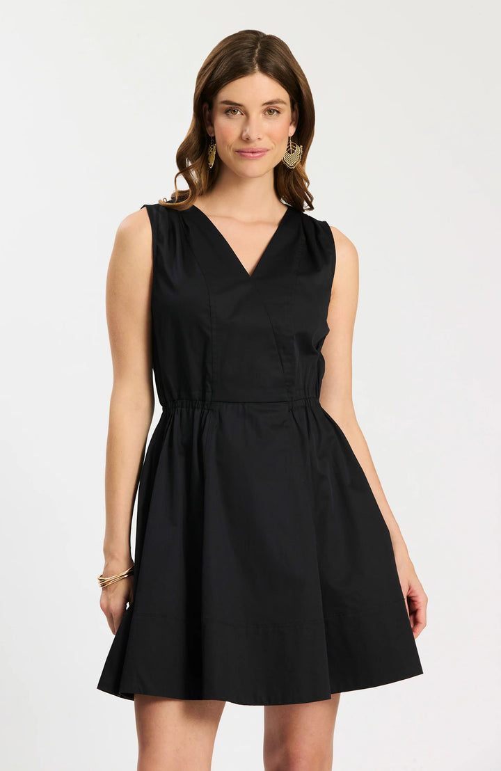 Model wearing Tyler Boe Emory Sleeveless Wrap Dress in black, front view belted with woven rattan belt, styled with black block-heel sandals and gold earrings, on white background.
