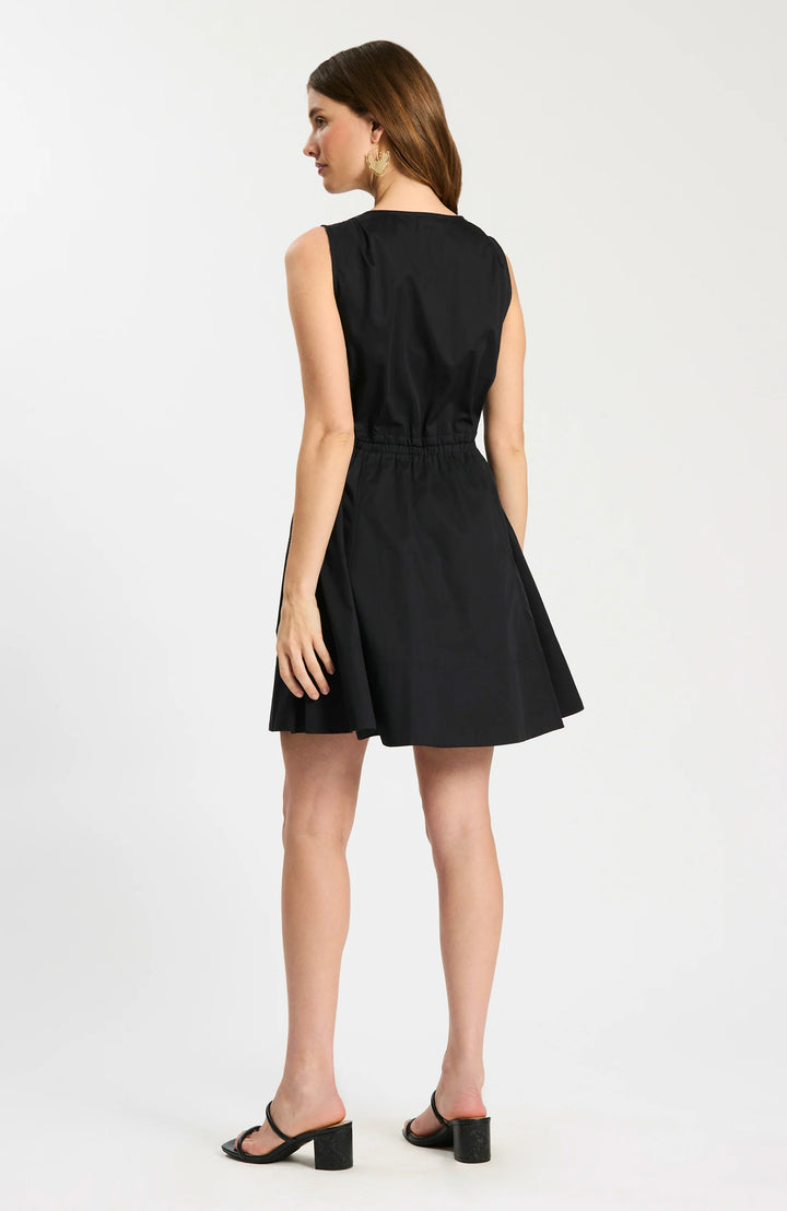 Model wearing Tyler Boe Emory Sleeveless Wrap Dress in black, front view belted with woven rattan belt, styled with black block-heel sandals and gold earrings, on white background. - back