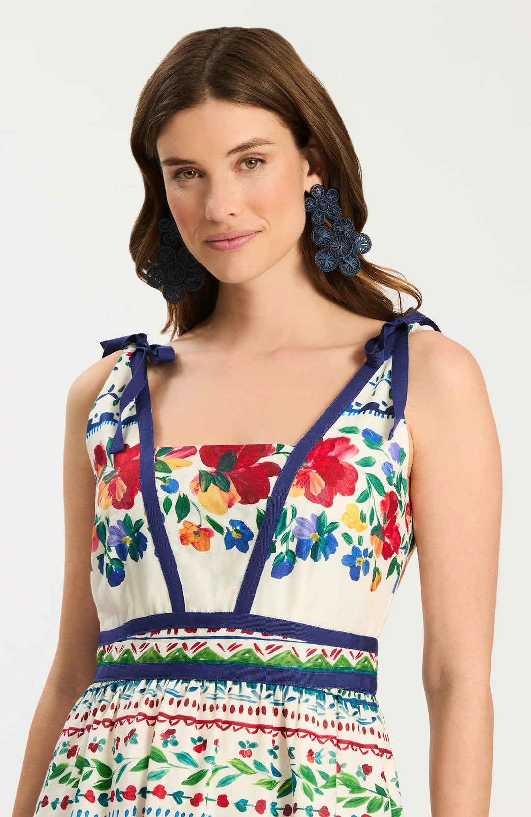 Tyler Boe Chelsey Cotton Summer Soiree Dress, close-up of bodice showing V-neckline with built-in modesty insert, navy grosgrain ribbon paneling, shoulder-tie bow straps, and watercolor floral print on ivory ground.