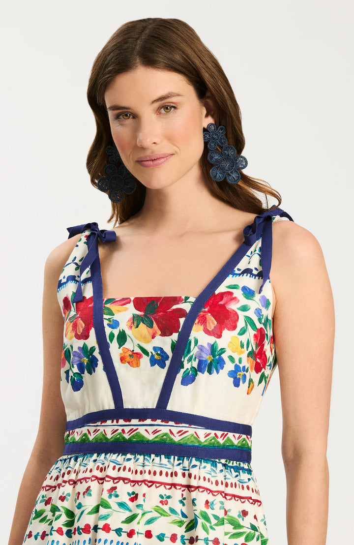 Tyler Boe Chelsey Cotton Summer Soiree Dress, close-up of bodice showing V-neckline with built-in modesty insert, navy grosgrain ribbon paneling, shoulder-tie bow straps, and watercolor floral print on ivory ground.