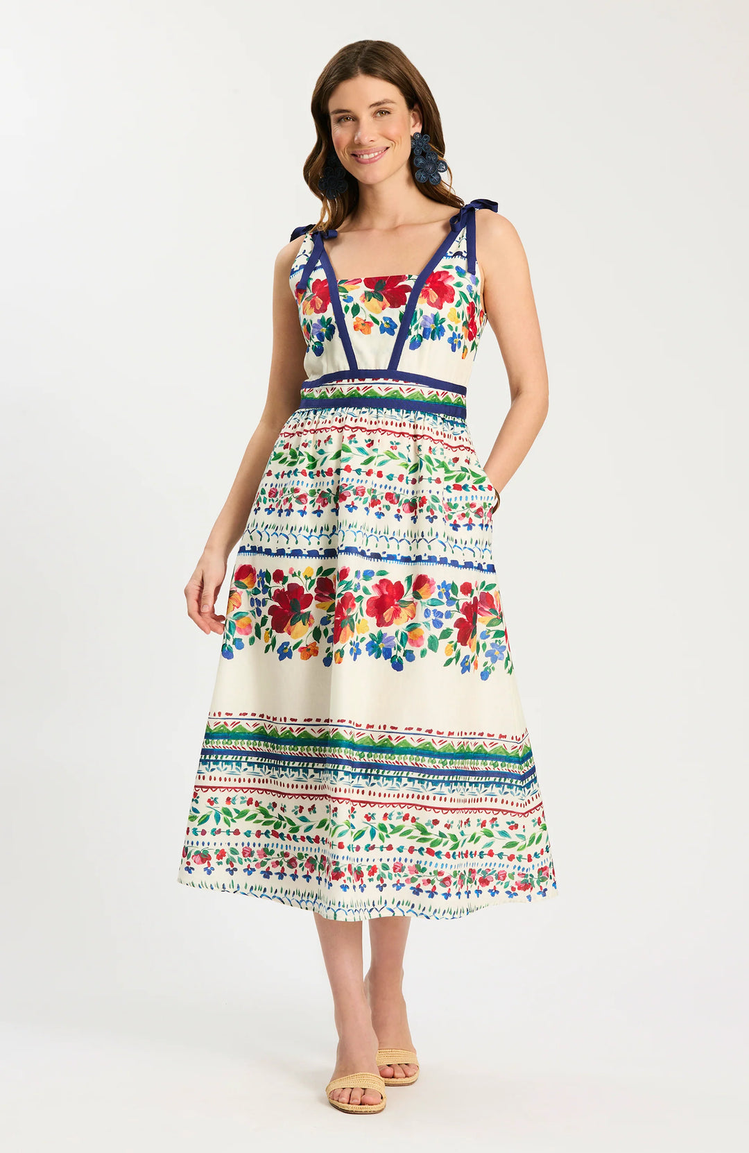 Tyler Boe Chelsey Cotton Summer Soiree Dress in ivory with multicolor painterly floral print and navy grosgrain trim, shown front on-model, square V-neckline with shoulder-tie straps, fitted bodice, full midi skirt with bordered print bands, styled with raffia slides.