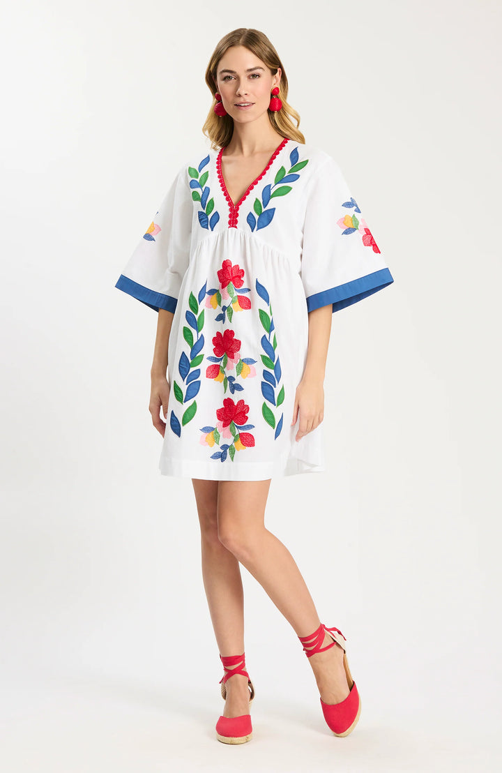 Tyler Boe Naomi Applique Dress in white with multicolor floral and leaf embroidered applique and blue contrast cuffs, shown front on-model, V-neckline with red scalloped picot trim, empire-gathered bodice, wide elbow-length sleeves, A-line skirt above the knee, styled with red espadrille wedges.