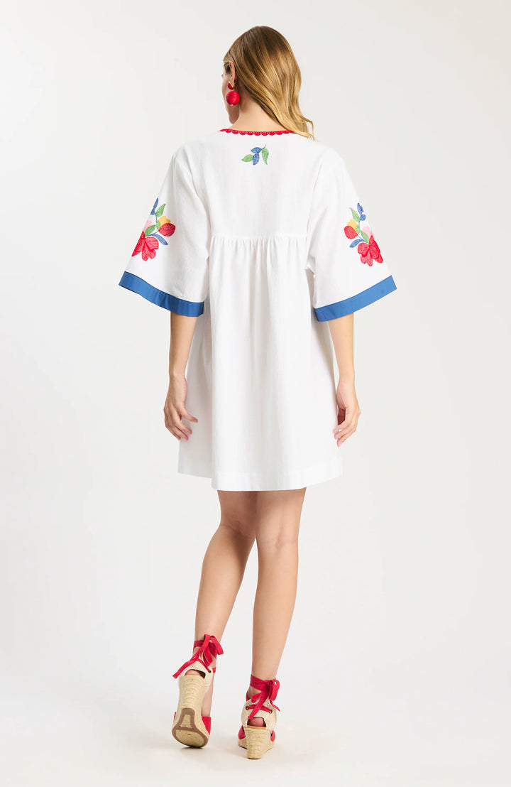 Tyler Boe Naomi Applique Dress, back view in white cotton with floral applique on the sleeves and blue cuff bands, showing the gathered empire back seam and relaxed A-line shape.