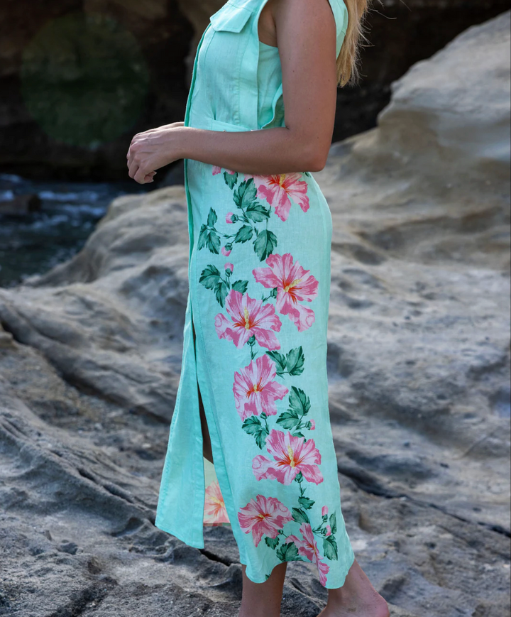 Person wearing a light green dress with pink floral patterns on a rocky beach.
