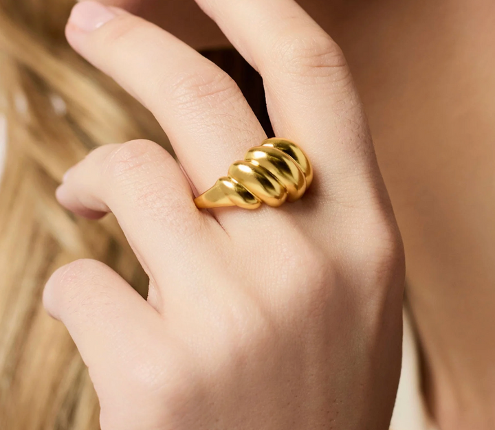 Close-up of a hand wearing the Ravello Ring, showing the polished gold ribbed spiral sitting high on the finger.