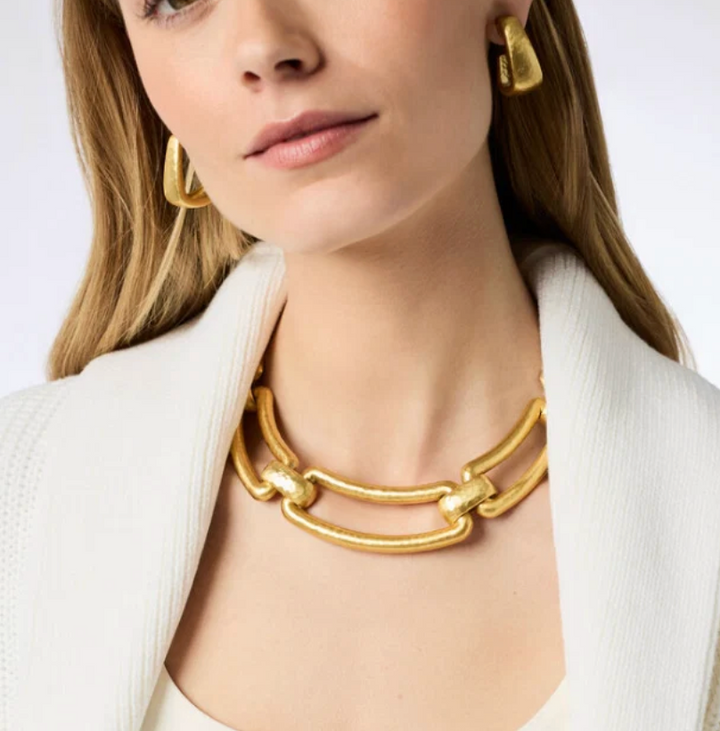 Close-up of a woman wearing the Sahara Collar Necklace with matching gold earrings over a white ribbed blazer.