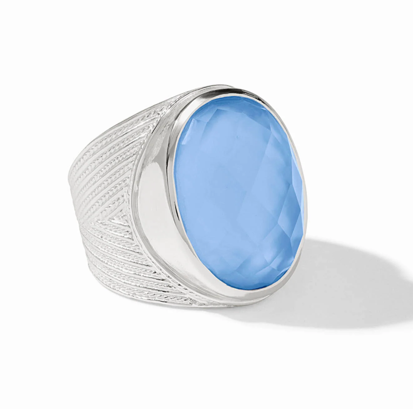 Julie Vos Verona Statement Ring in silver plate — wide chevron-etched band with large oval faceted chalcedony blue glass stone in bezel setting, on white background.