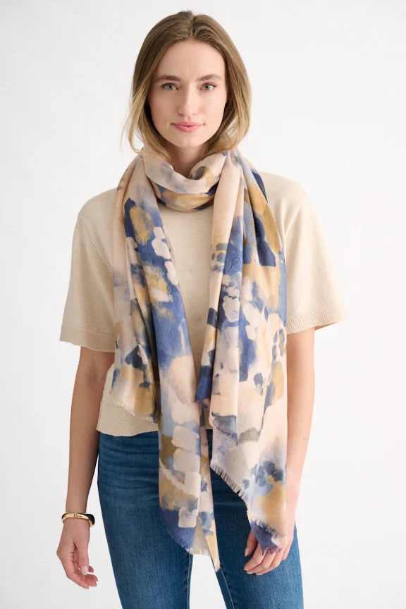 Woman wearing a navy multi abstract print scarf knotted over a beige sweater.