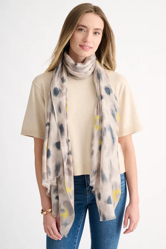 Woman wearing a grey and yellow painted leopard print scarf over a beige sweater.