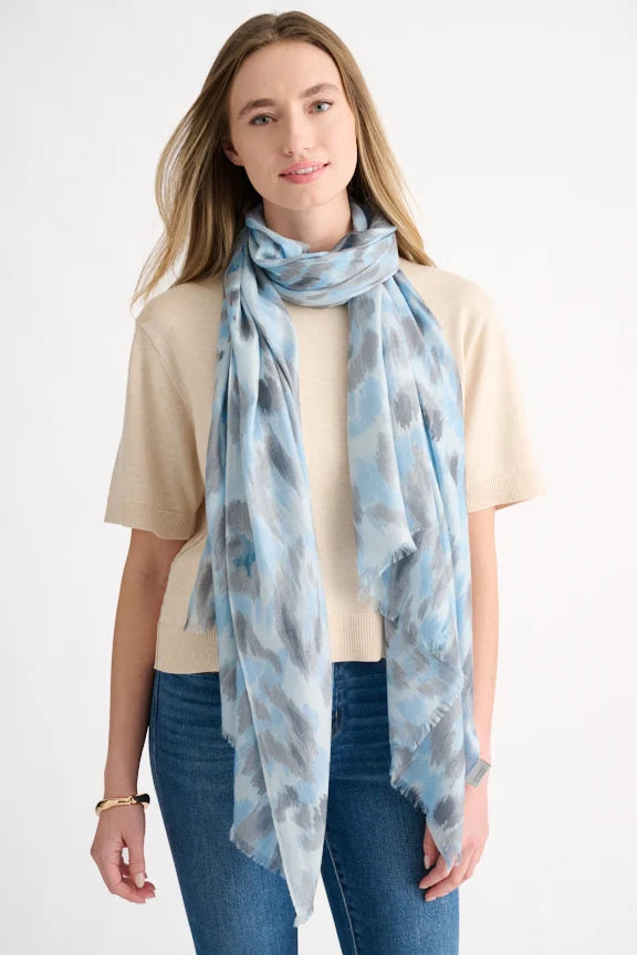 Woman wearing a blue and grey painted leopard print scarf over a beige sweater.