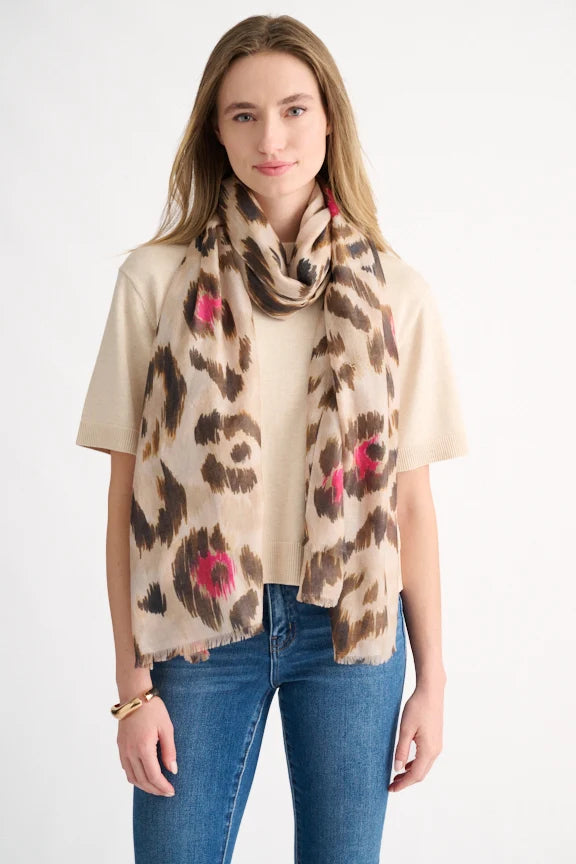 Woman wearing a neutral and pink painted leopard print scarf over a beige sweater.