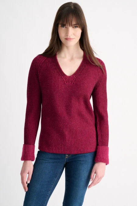 Woman wearing a cranberry plaited rib V-neck cashmere sweater with folded cuffs, paired with jeans.