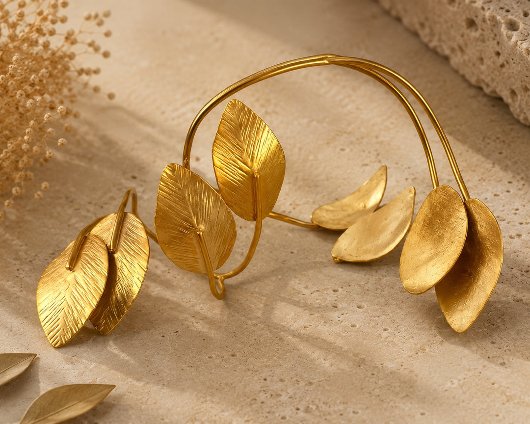 Front/hero shot — LION Gold Leaf Cuff Bracelet by Ximena Castillo, 24k gold-plated bronze double-band cuff with leaf charm clusters on natural stone surface