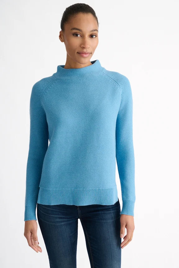 Woman wearing a blue garter knit funnel neck sweater with jeans.