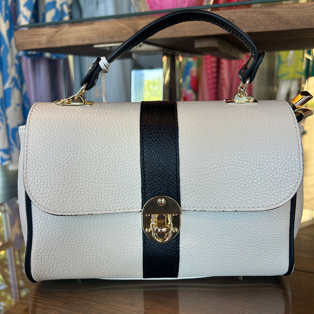 White handbag with a black strap and gold clasp on a wooden surface.