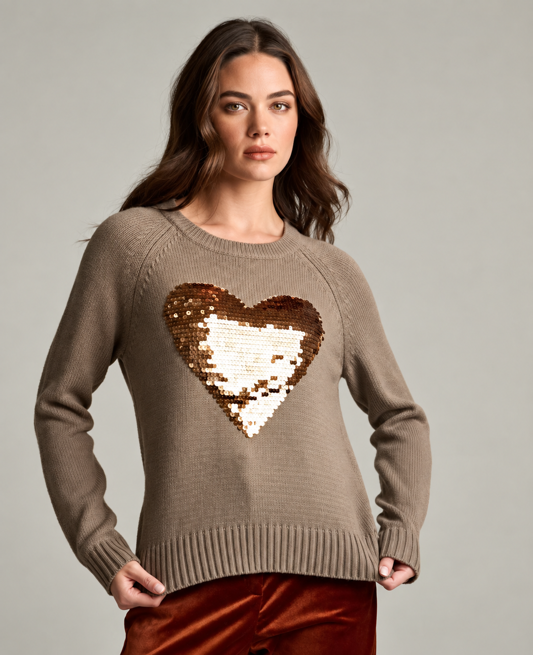 ront view of a woman wearing the Love Shine Sweater in reed, a taupe knit crewneck sweater with an oversized sequin heart appliqué in gold and bronze tones on the chest.