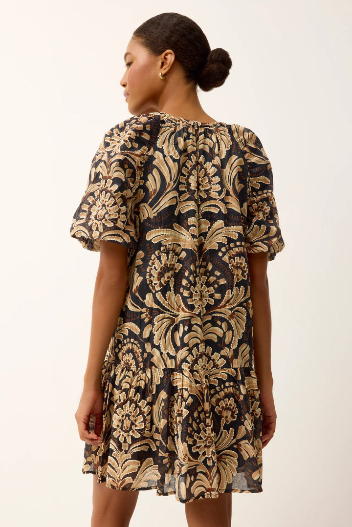 Marie Oliver Greta Tropez Dress in dark navy and gold medallion print — back on-model view showing gathered smocked neckline with button closure, tiered skirt hem, and full print layout