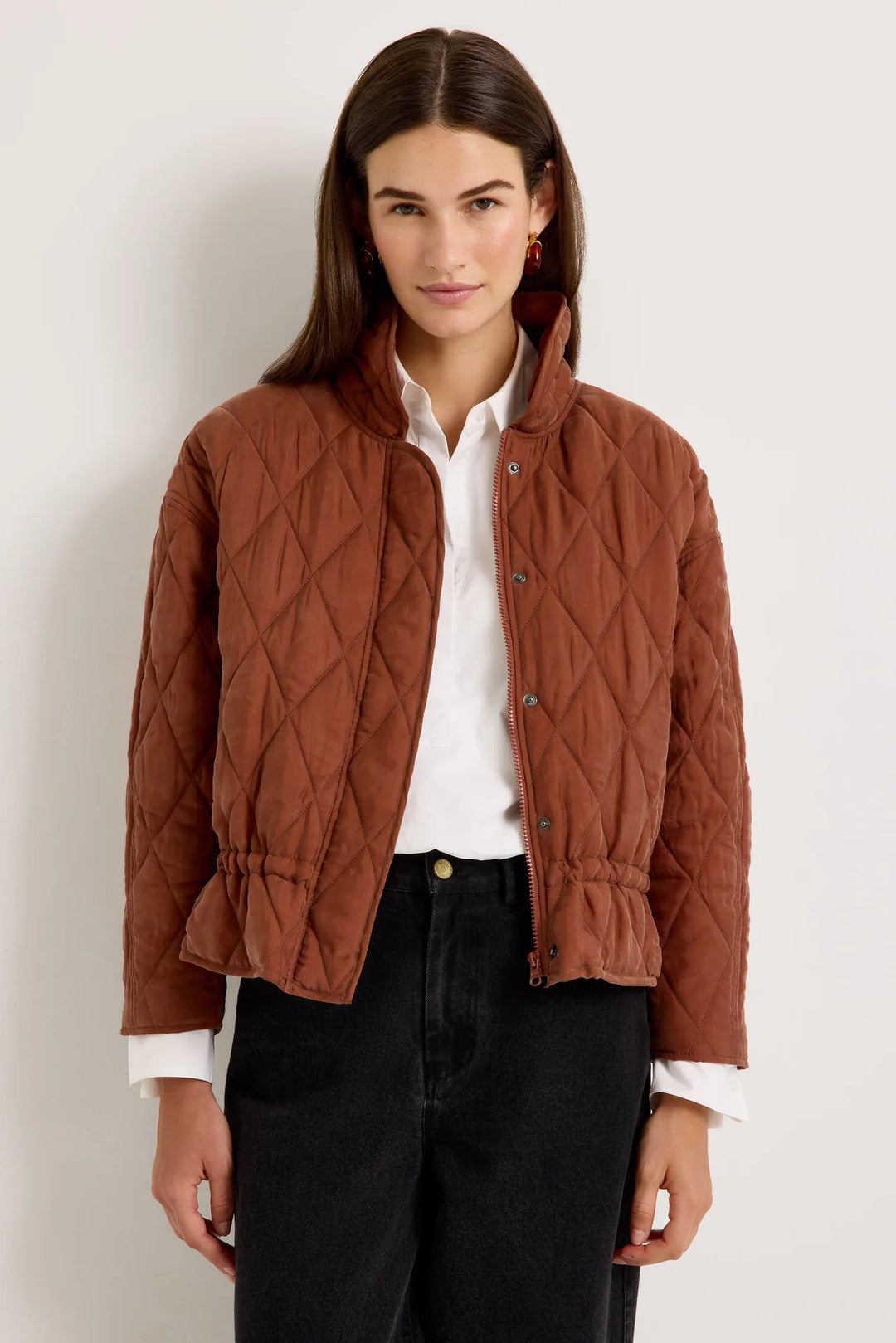 Marie Oliver Haisley Jacket in Tortoise, front view on model, worn unzipped showing diamond quilting, funnel neck, snap placket, and drawstring waist over a white button-down and black jeans
