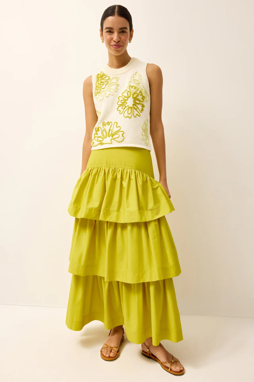 Front full-length view of a cropped cream sleeveless knit top featuring large-scale floral embroidery in chartreuse, styled with a matching chartreuse tiered ruffle maxi skirt and tan flat sandals.