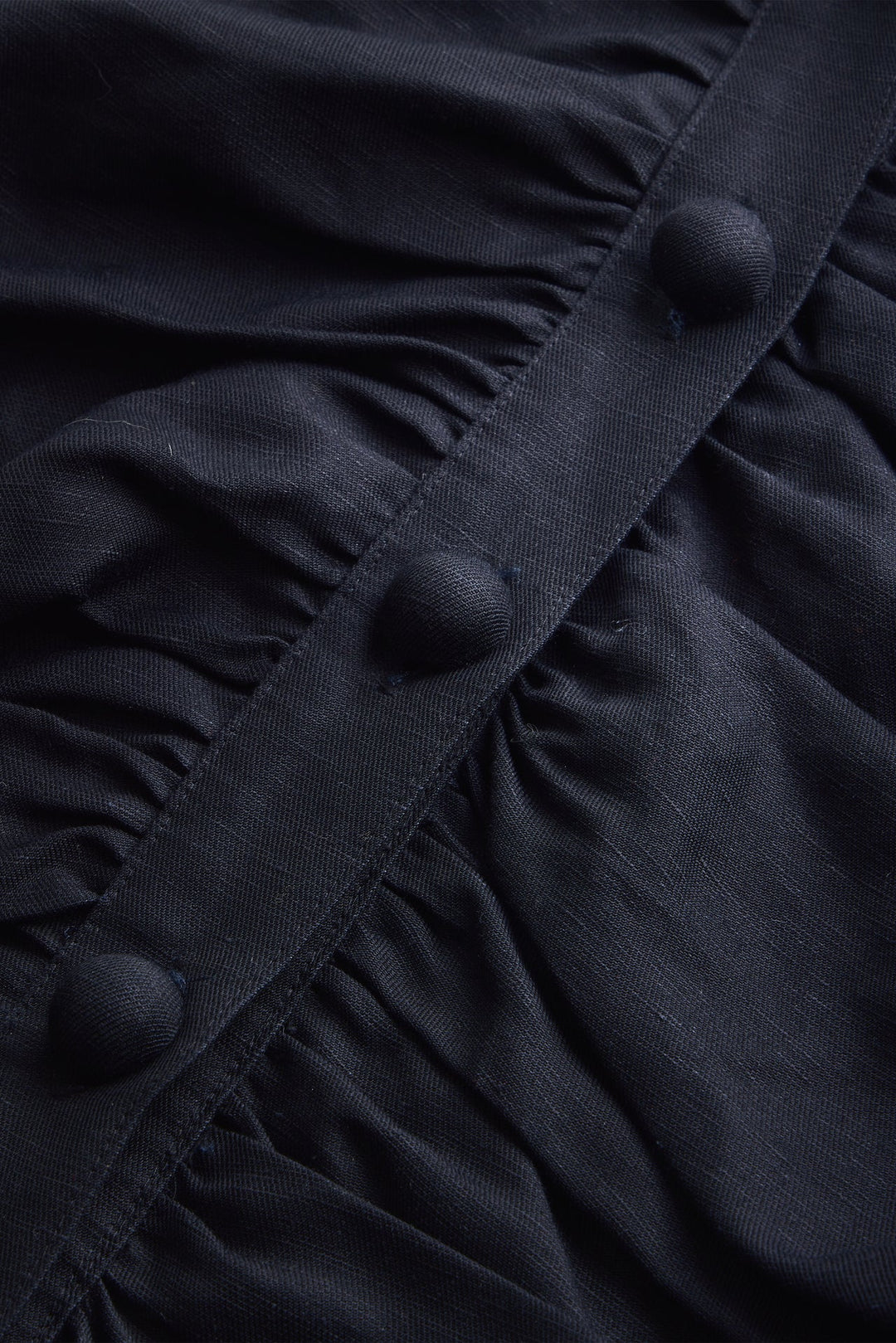Closeup of Marie Oliver Rowan Top in Black —  with oversized statement buttons, ruched bodice panels, puff sleeves, and cropped fit styled with matching shorts and black tank.