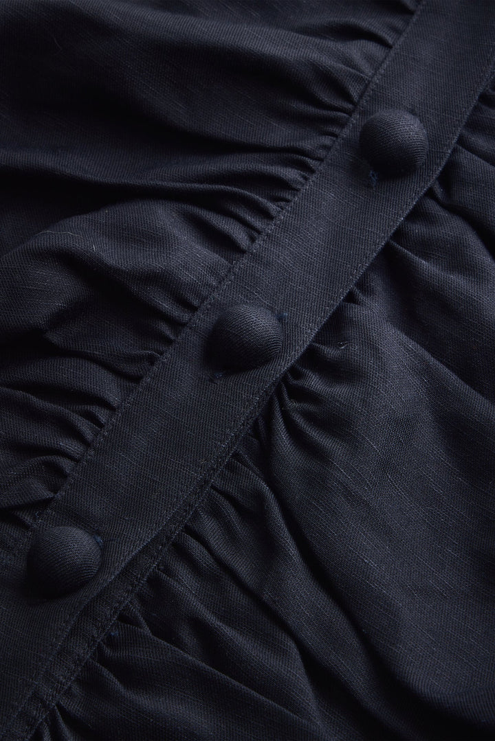 Closeup of Marie Oliver Rowan Top in Black —  with oversized statement buttons, ruched bodice panels, puff sleeves, and cropped fit styled with matching shorts and black tank.