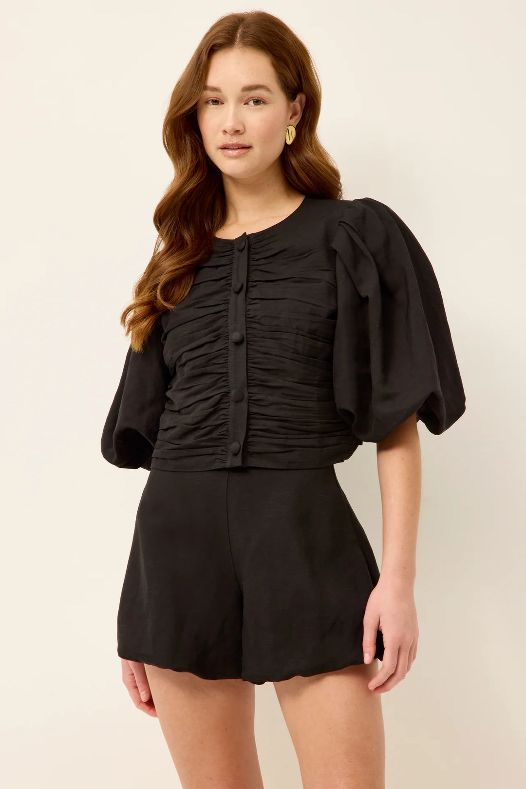 Marie Oliver Rowan Top in Black — front view showing open button closure with oversized statement buttons, ruched bodice panels, puff sleeves, and cropped fit styled with matching shorts and black tank.