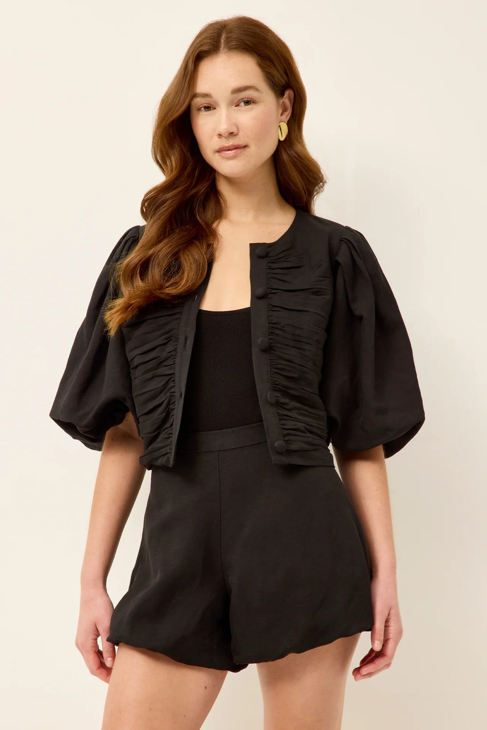 Marie Oliver Rowan Top in Black — front view showing open as a jacket with oversized statement buttons, ruched bodice panels, puff sleeves, and cropped fit styled with matching shorts and black tank.