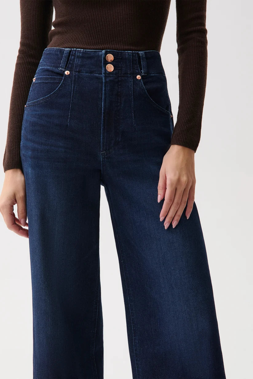 Close-up of dark wash denim waistband showing double rose-gold button closure and front pockets.