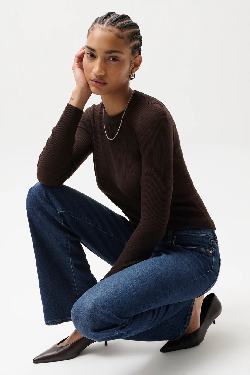 Woman wearing a brown long-sleeve top and blue jeans on a white background