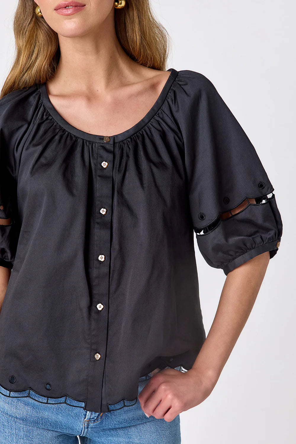 Closeup of Crosby Perrie Top in black, styled with a gathered scoop neckline, balloon sleeves, and button front, worn with medium-wash denim.