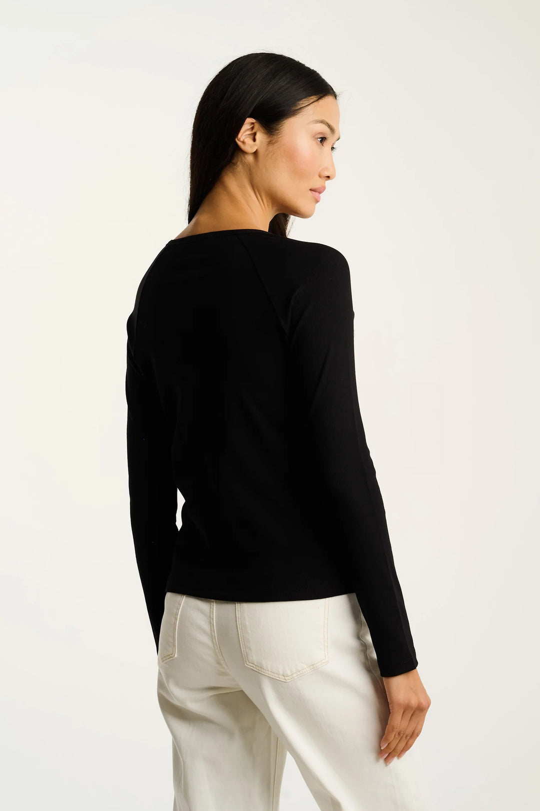 Woman wearing a black long-sleeve top and white pants on a white background