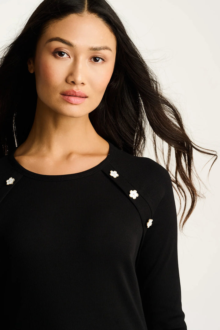Woman wearing a black top with white floral embellishments on a plain background