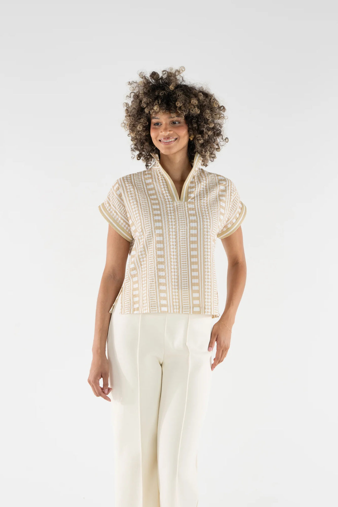 Emily McCarthy Riviera Top in Piazza Stripe, sand and white geometric vertical stripe cotton top with stand collar and dolman sleeves, shown tucked into white wide-leg trousers.