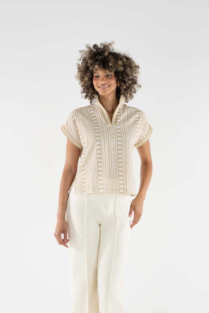 Emily McCarthy Riviera Top in Piazza Stripe, sand and white geometric vertical stripe cotton top with stand collar and dolman sleeves, shown tucked into white wide-leg trousers.