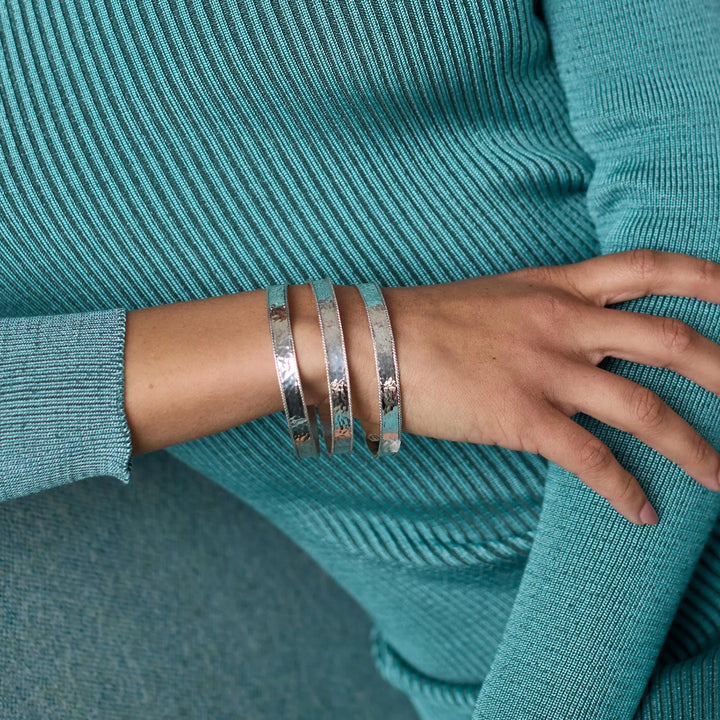 Model wearing 3 Julie Vos Savoy Bangle in silver plate with hammered face and rope-edge detail.
