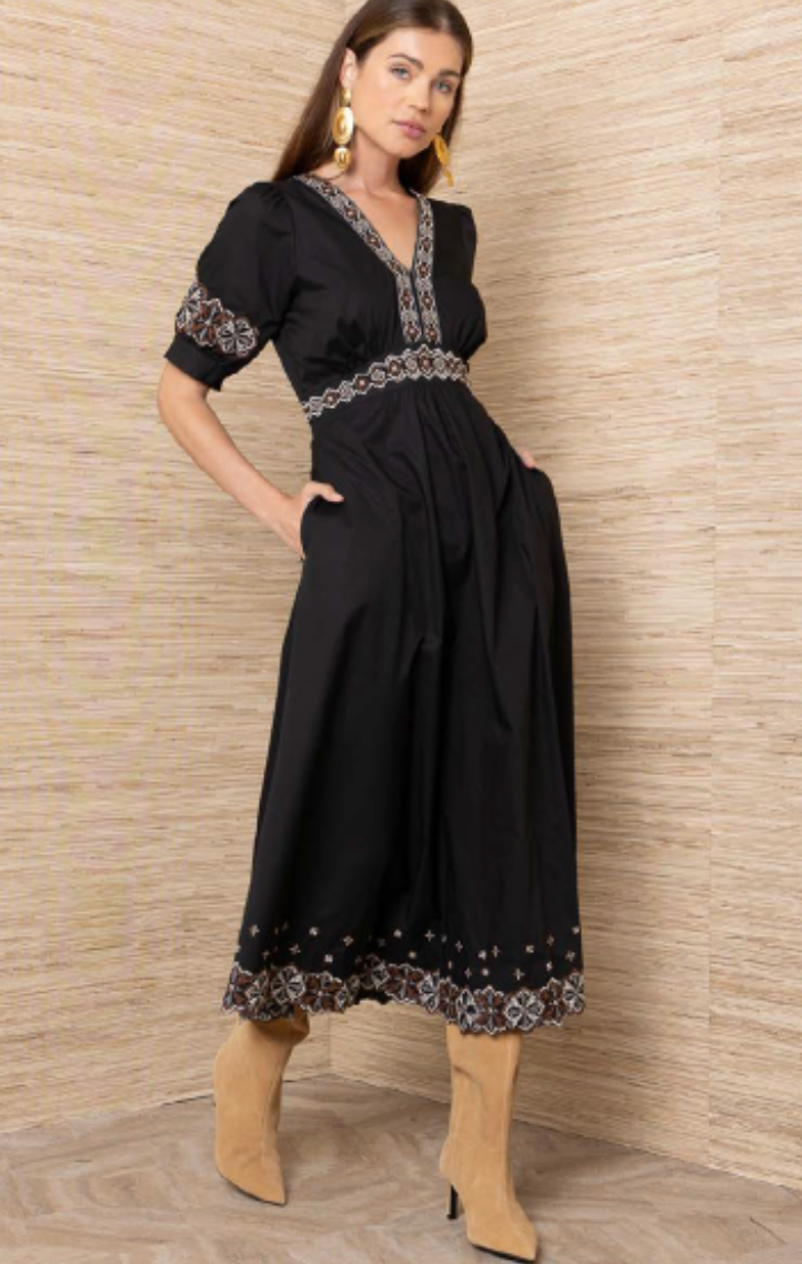 Black poplin midi dress with geometric embroidery at neckline, empire waist, cuffs, and hem, shown on model with tan boots.