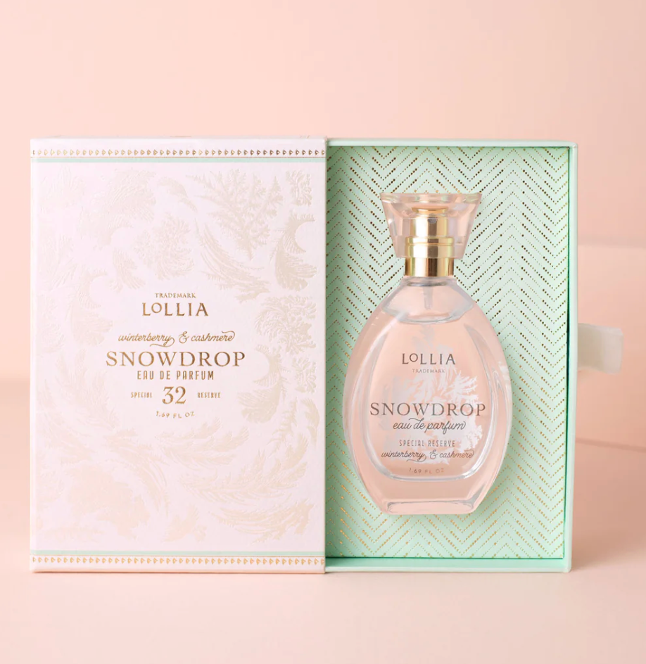 Lollia Snowdrop Eau de Parfum in a teardrop glass bottle with gold pump, nestled in a mint and gold slide-open gift box with etched frost pattern, shown against a blush background.