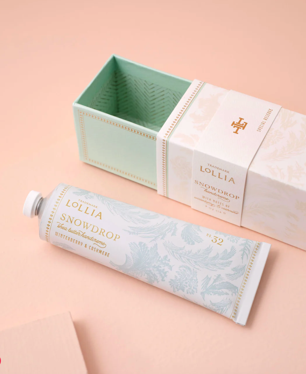 Lollia Snowdrop Handcreme tube beside its open slide-out keepsake box showing mint and gold chevron interior lining.